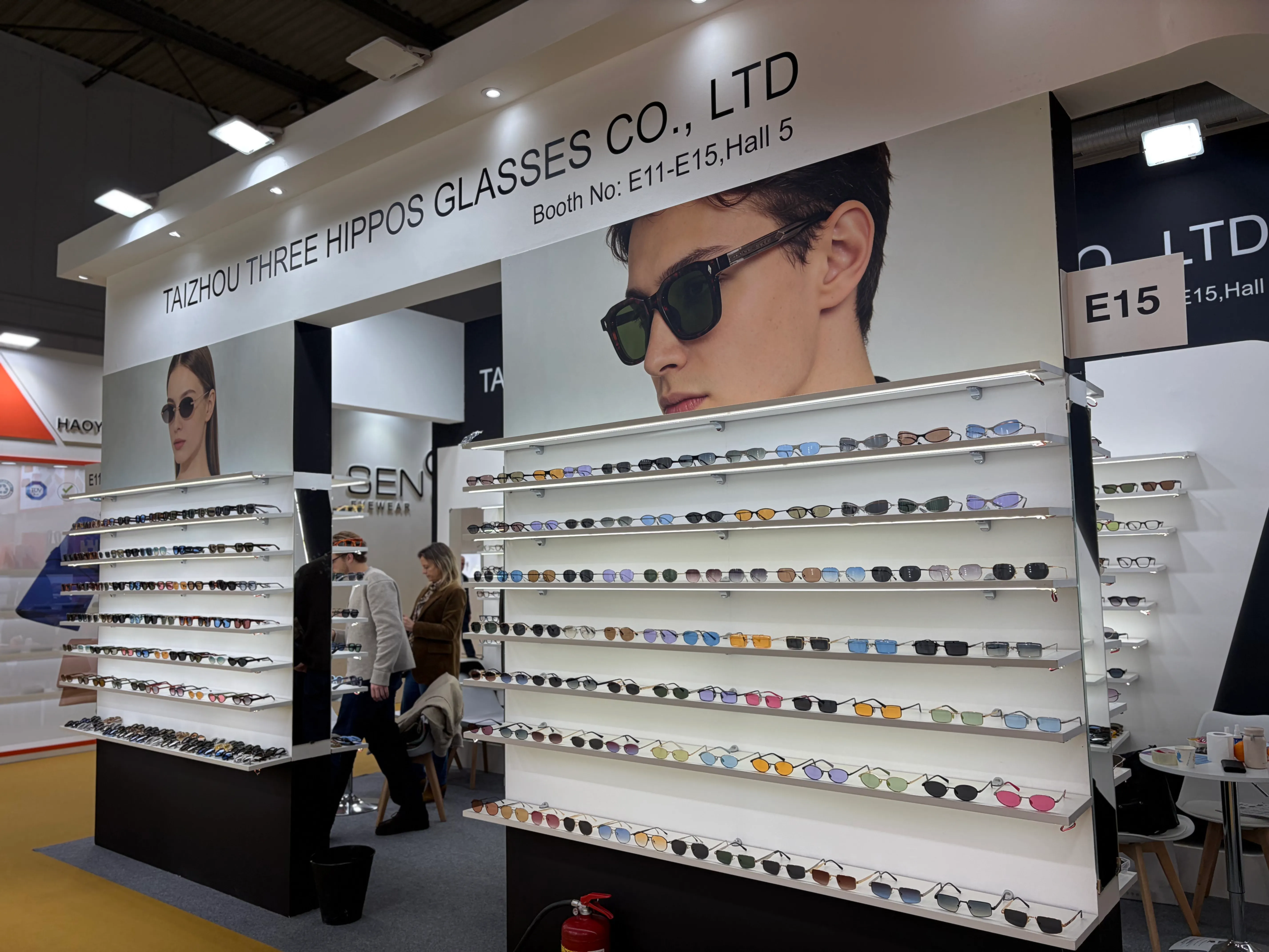 Three Hippos booth E11-E15, Hall 5 at the MIDO eyewear show in Milan 2025, with wall-mounted sunglasses displays and visiting buyers